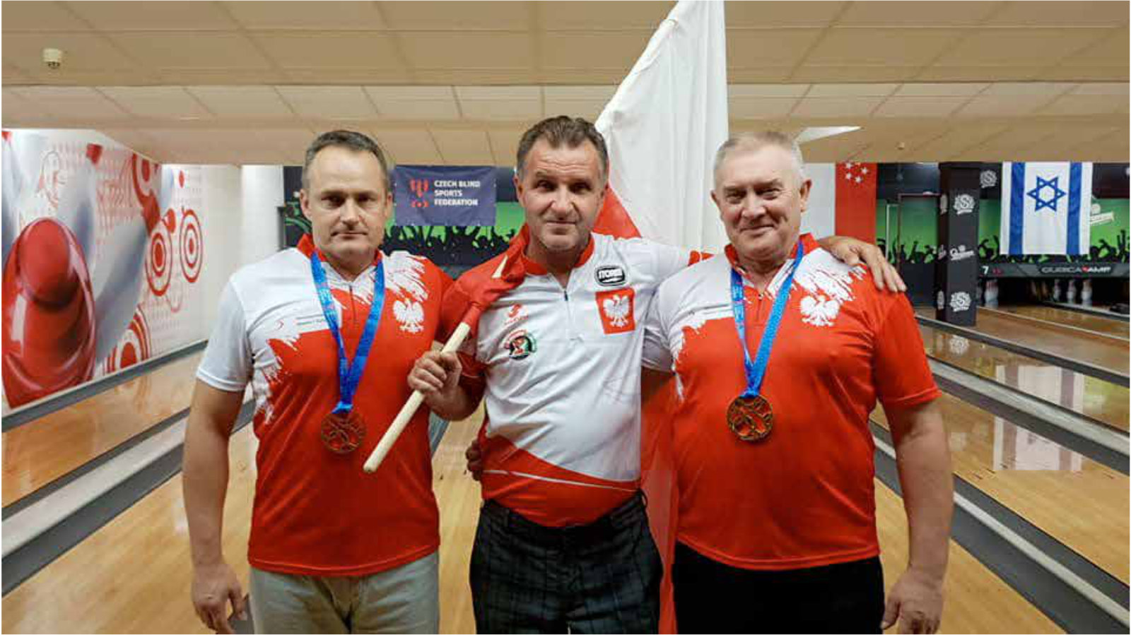 Mężczyźni z z medalami i flagą polski, w tle tor bowlingowy